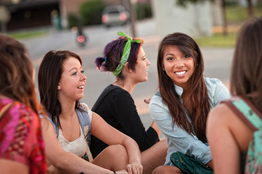 5 gut gelaunte junge Frauen, die an einer Straße sitzen